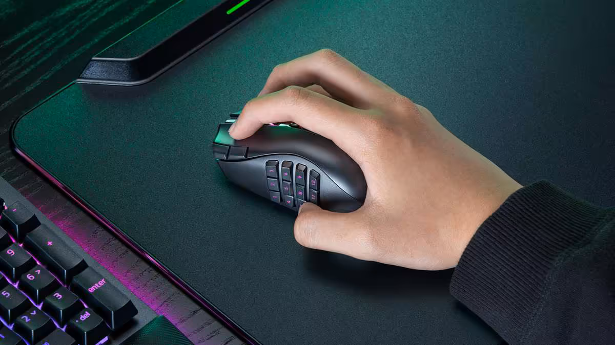 Main tenant la souris Razer Naga V3 Pro avec pavé latéral MMO sur tapis de bureau