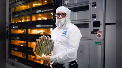 Technicien Intel en salle blanche tenant un wafer de puce devant des équipements de fabrication de semi-conducteurs