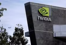 Façade d’immeuble NVIDIA avec logo vert sur mur gris, ciel nuageux et arbre au premier plan