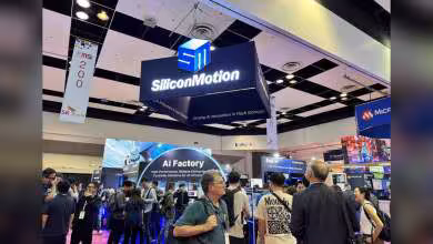 Stand Silicon Motion en salon tech avec grand logo suspendu et visiteurs devant un écran AI Factory