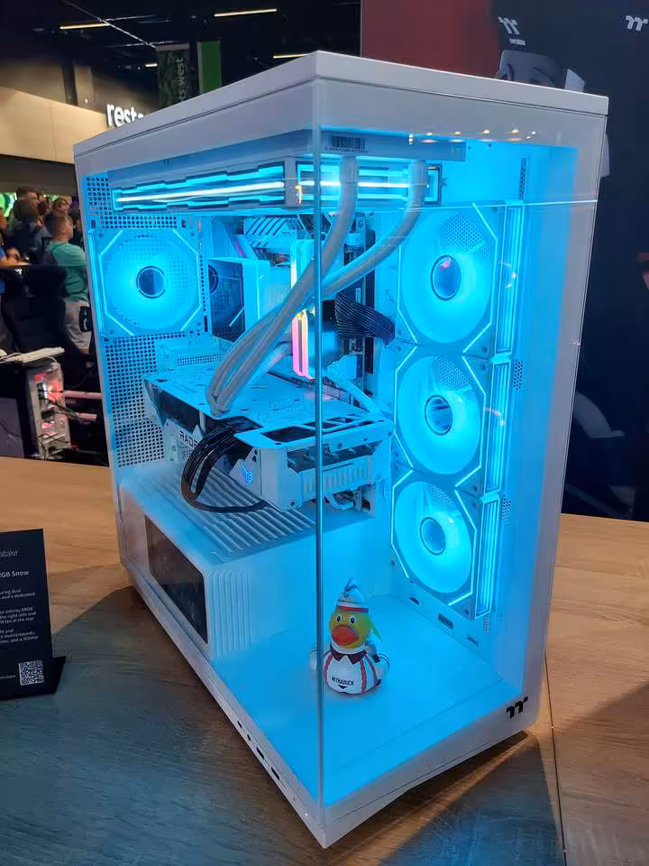 Thermaltake Gamescom 2026 : CAPO X, Stage 450 TG et alimentations DockPower 15 Boîtier Thermaltake blanc vitré, trois ventilateurs latéraux RGB bleus et tuyaux de watercooling.