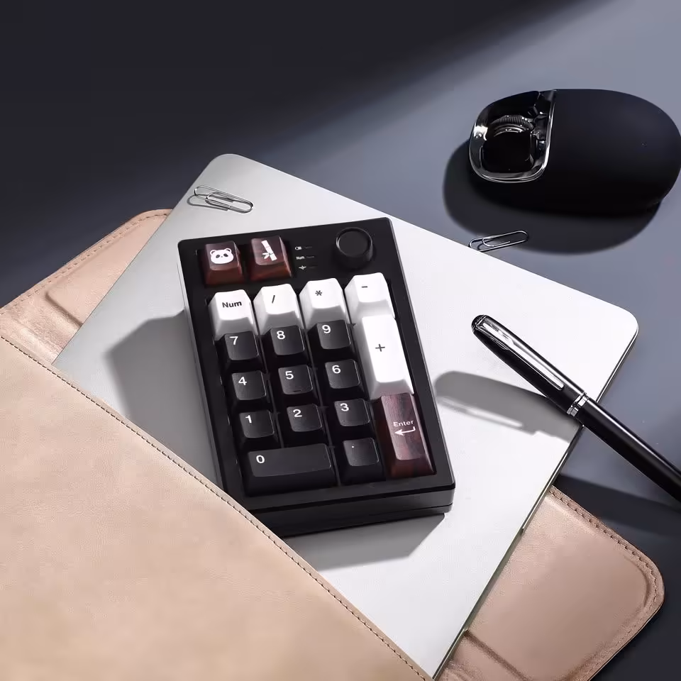 Yunzii AL21 : un pavé numérique aluminium sans fil à 49,99 dollars pour claviers compacts 17 Yunzii AL21 noir avec keycaps bicolores, posé sur un ordinateur portable avec souris et stylo