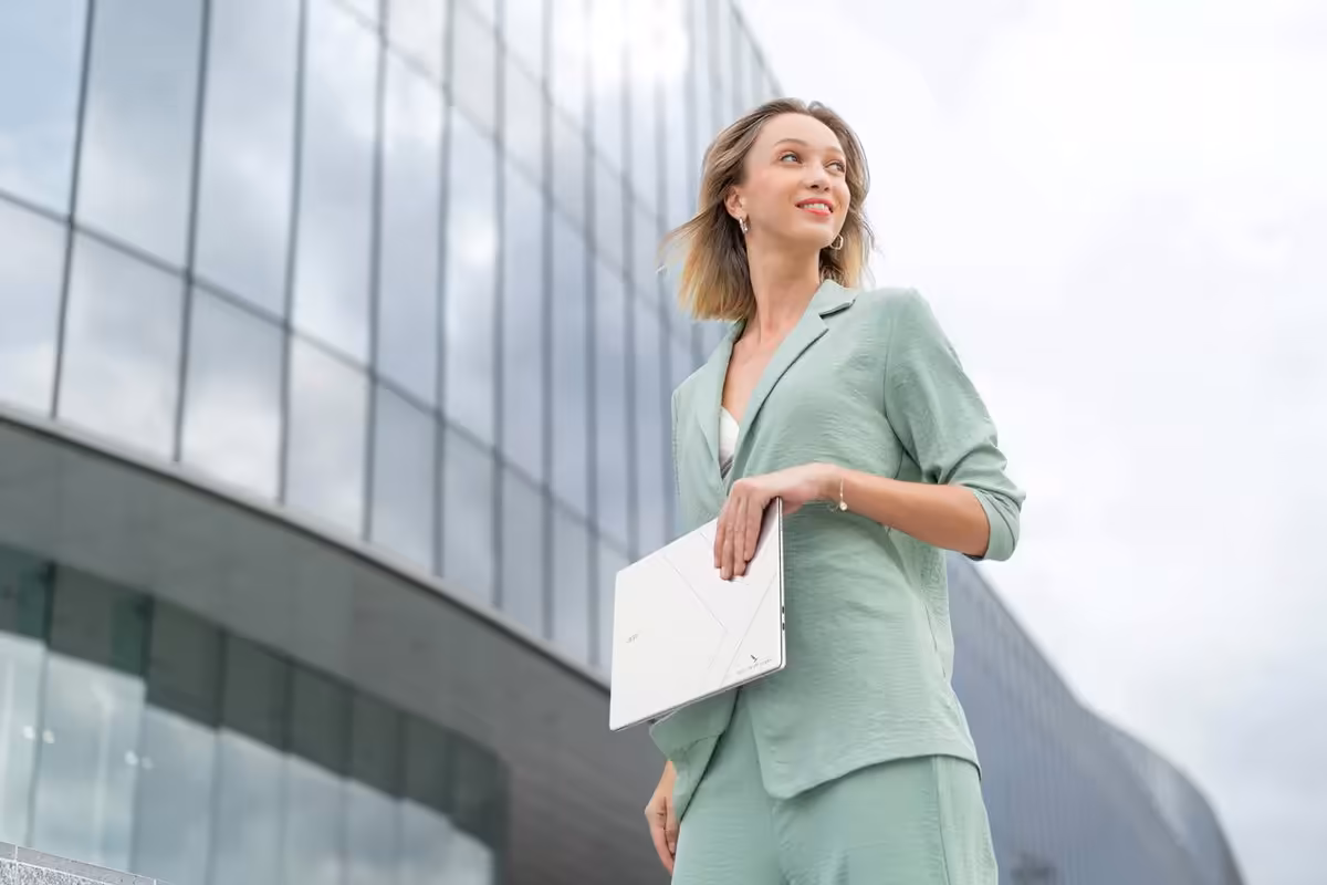Femme tenant un ordinateur portable Acer blanc devant un immeuble vitré moderne