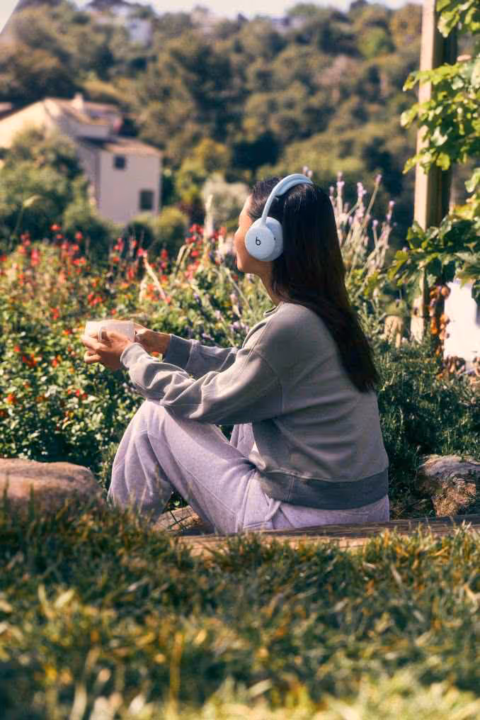 Beats 360 : le casque modulable mise sur l’ANC, le confort et 32 heures d’autonomie 9 Femme portant un casque Beats 360 blanc assise dans un jardin