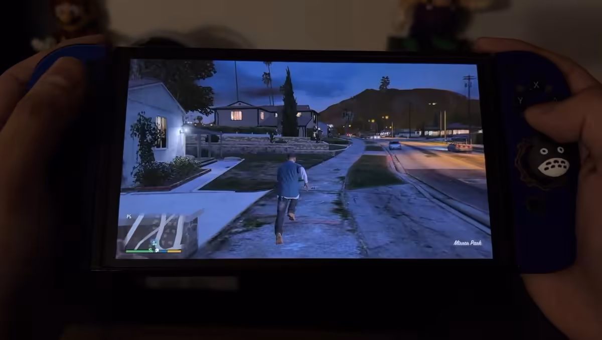 GTA 5 sur Nintendo Switch : un port natif amateur tourne sur la console d'origine 3 Nintendo Switch OLED bleue montrant GTA 5 en vue troisième personne dans une rue résidentielle nocturne