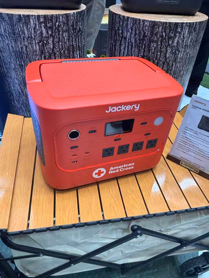Station portable Jackery rouge avec logo Jackery, écran, prises AC et badge American Red Cross sur table