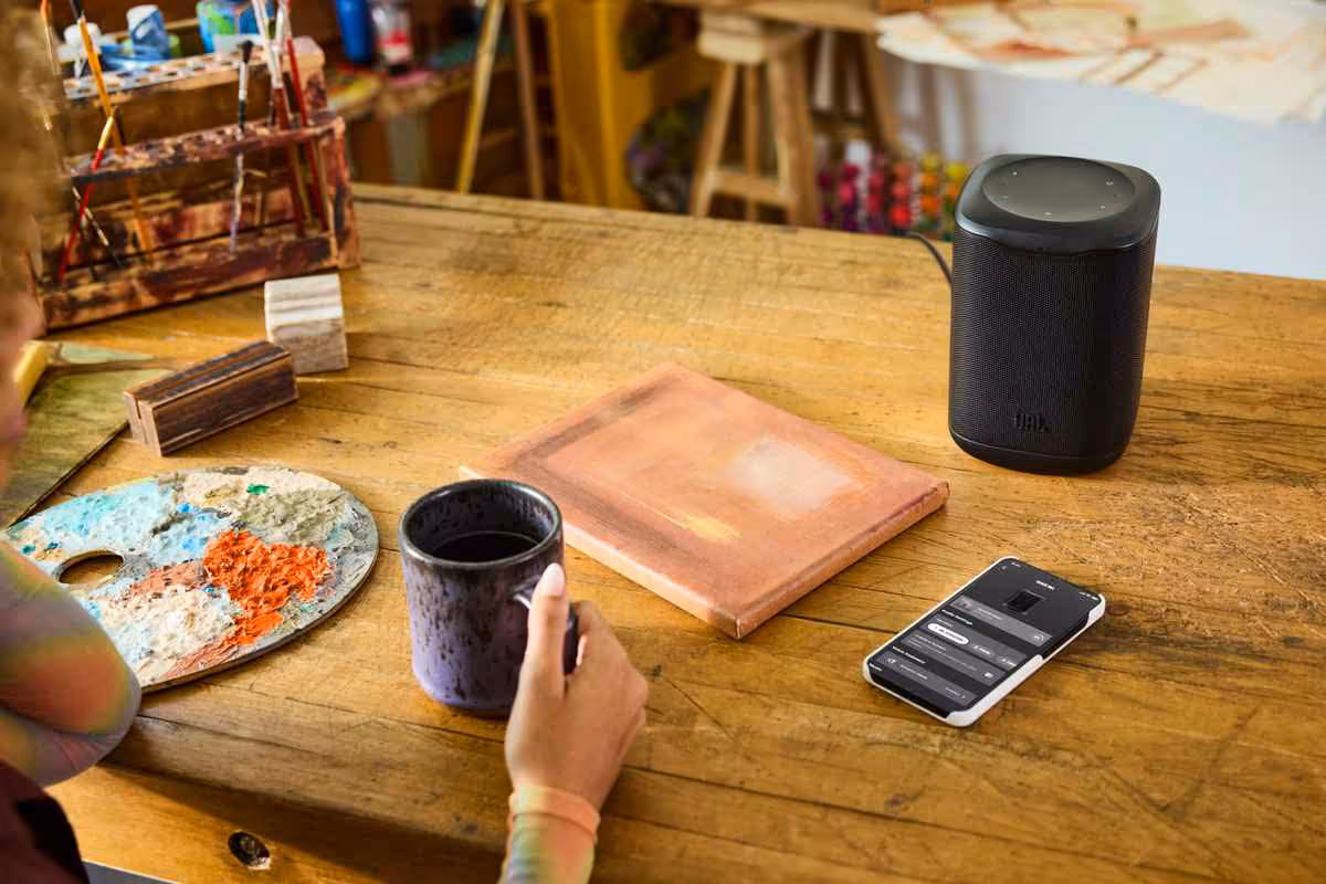 Enceinte JBL Cove noire dans un atelier, reliée à un smartphone et posée près de matériel créatif.