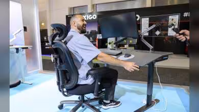 Chaise ergonomique Huanuo avec bureau assis-debout et bras d’écran, utilisateur devant deux moniteurs au salon IFA