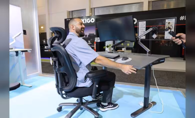 Huanuo IFA 2026 : chaises, bureaux et bras d’écran misent sur l’ergonomie intelligente 1 Chaise ergonomique Huanuo avec bureau assis-debout et bras d’écran, utilisateur devant deux moniteurs au salon IFA