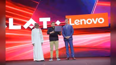 Trois hommes sur scène devant le logo Lenovo, l’un présentant un PC portable Lenovo brun foncé ouvert
