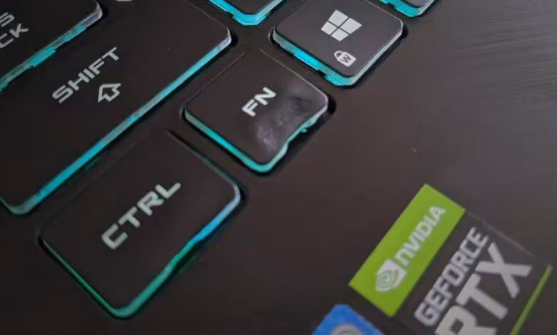 PC portable gaming : un sèche-cheveux de 2 000 W déforme une touche du clavier 1 Gros plan sur clavier de PC portable gaming avec touches rétroéclairées turquoise et autocollant NVIDIA GeForce RTX