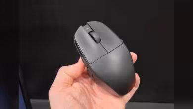 Souris sans fil noire vue de dessus, tenue en main, avec molette centrale et boutons principaux visibles
