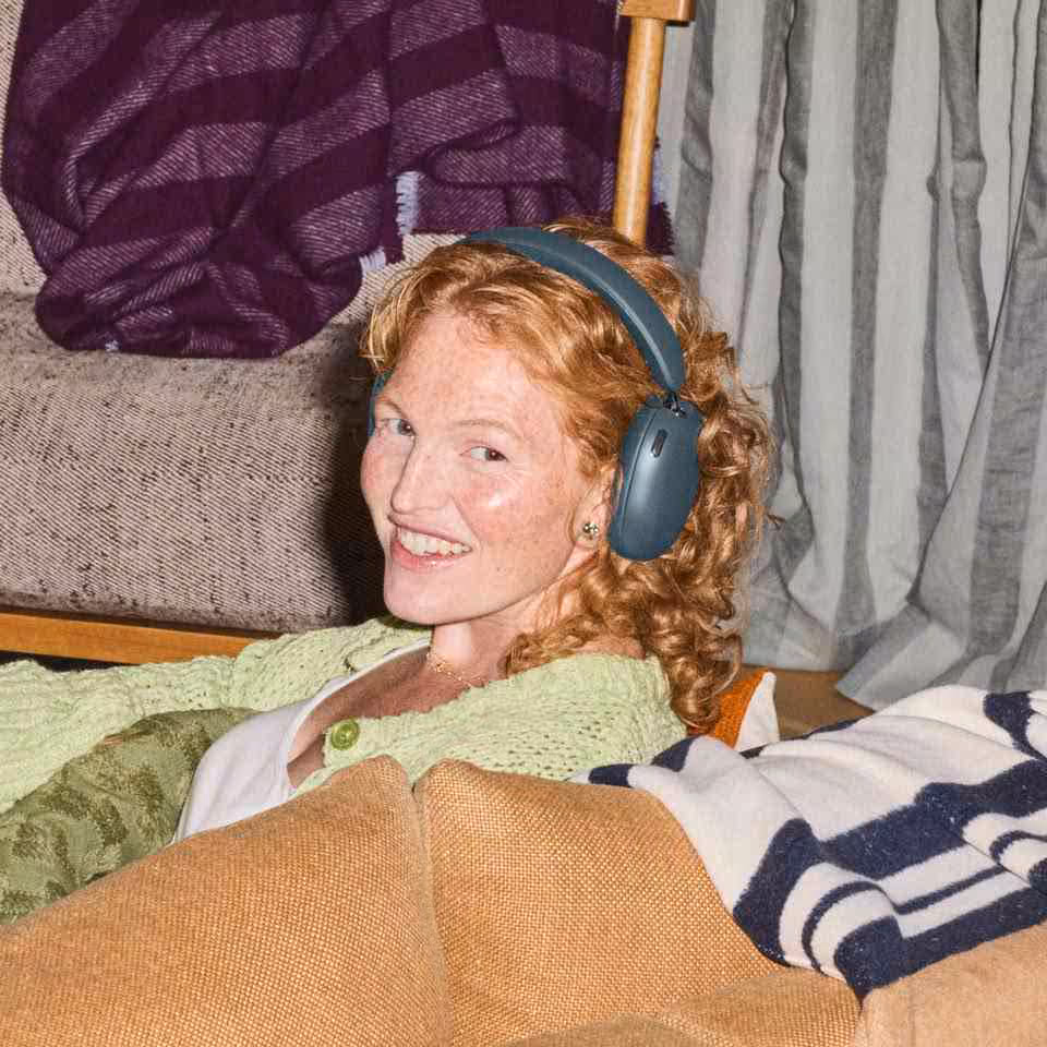Personne portant un casque Sonos bleu, allongée sur un canapé dans un intérieur cosy