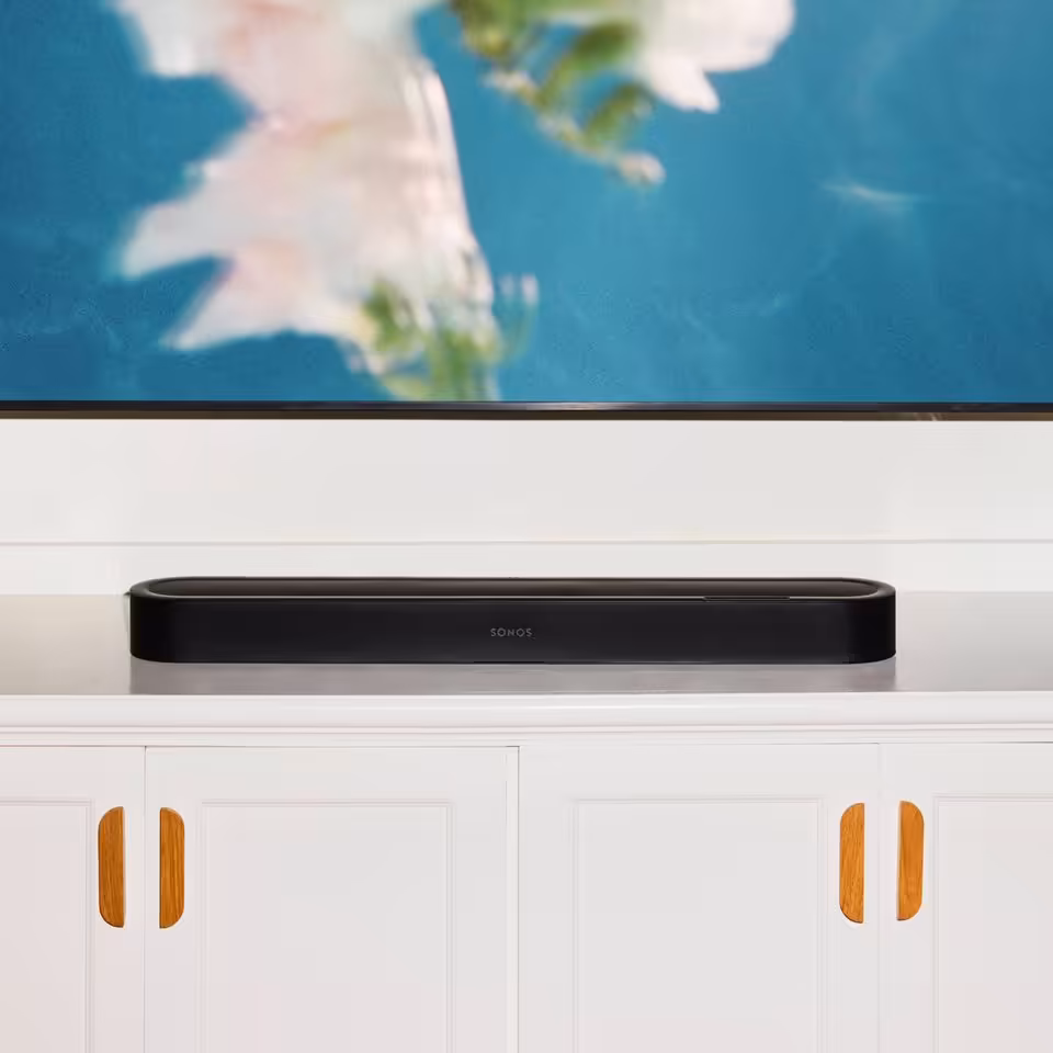 Barre de son Sonos noire posée sur un meuble blanc sous une télévision
