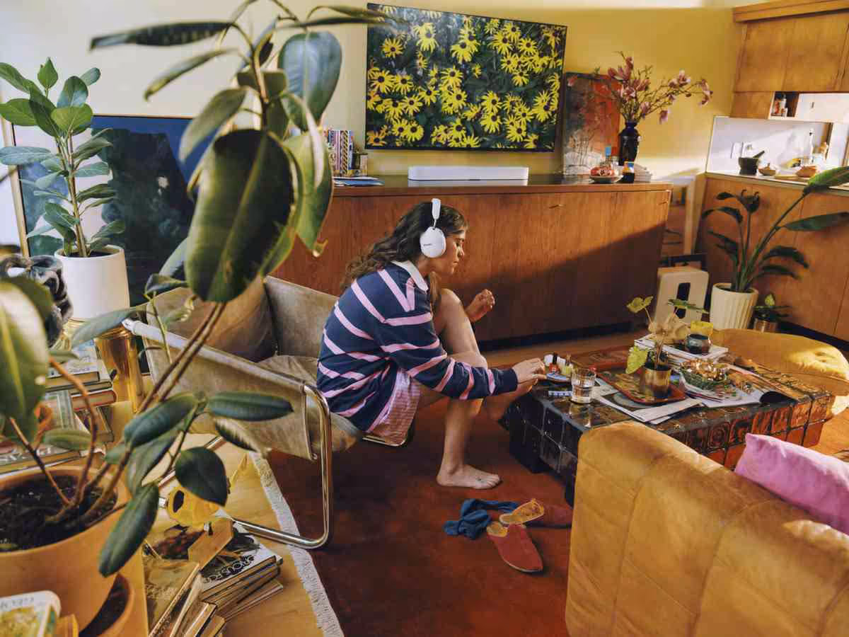 Personne dans un salon avec télévision, plantes et mobilier vintage, portant un casque Sonos blanc
