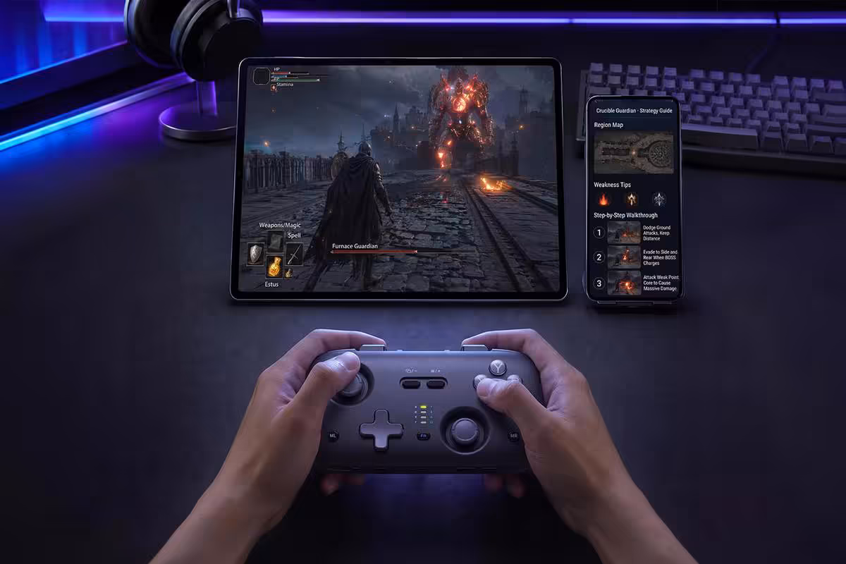 Joueur tenant une manette Voidjoy devant tablette, smartphone et setup gaming sur bureau
