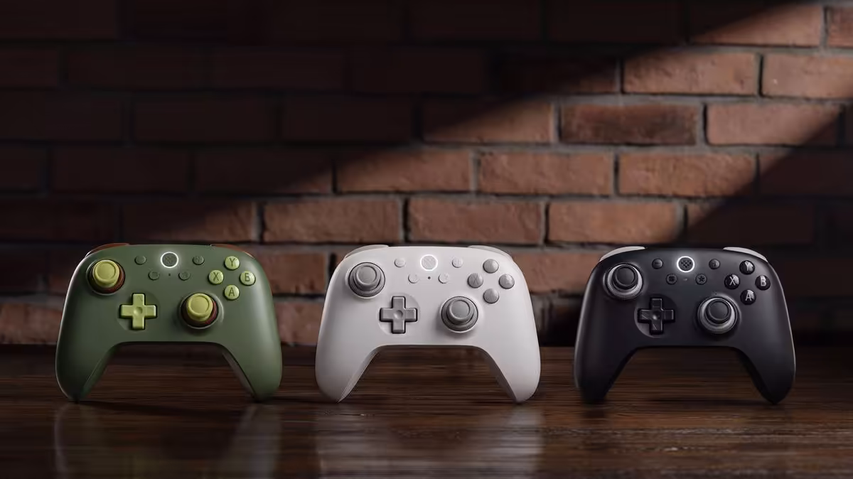 Trois manettes 8BitDo Ultimate 3C+ vert, blanc et noir devant un mur en briques