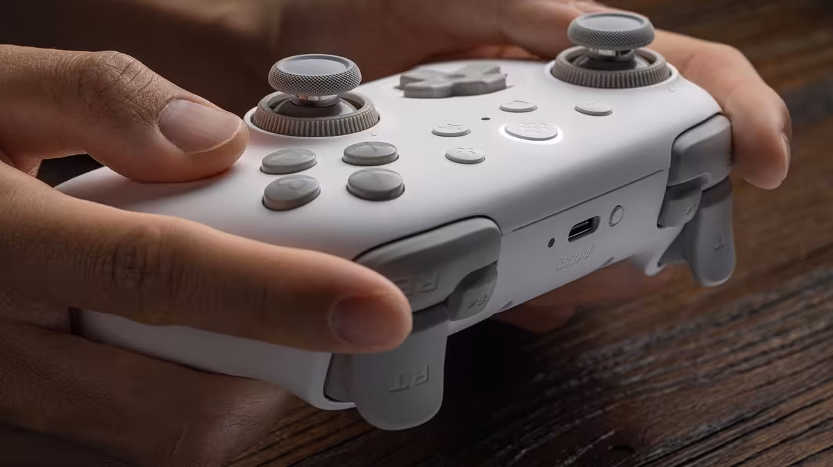 Manette 8BitDo Ultimate 3C+ blanche tenue en main sur un bureau en bois
