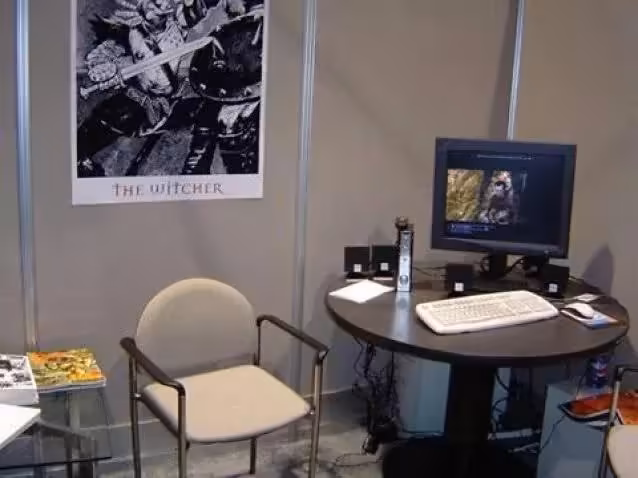 Stand de salon CD Projekt avec poster The Witcher, écran CRT, ordinateur et bureau rond