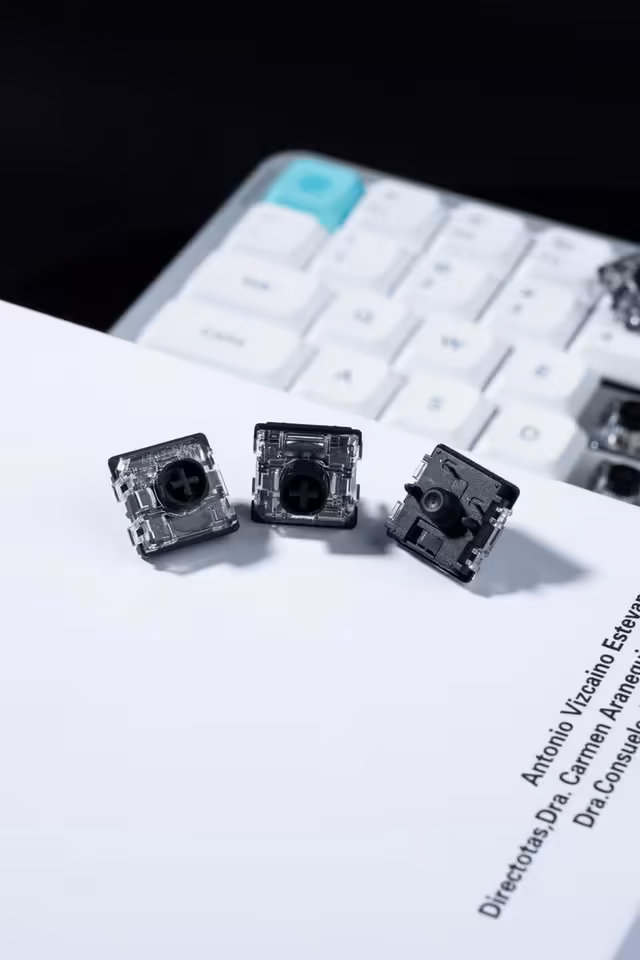 Gateron Low Profile Silent 3.0 Black : un switch discret au format 5 broches 2 Trois switches Gateron Low Profile Silent 3.0 Black devant un clavier mécanique blanc