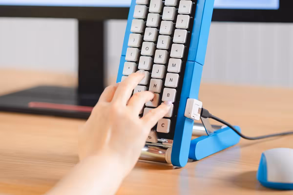 Main utilisant le clavier vertical Gboard Conveyor Belt bleu, connecté en USB sur un bureau