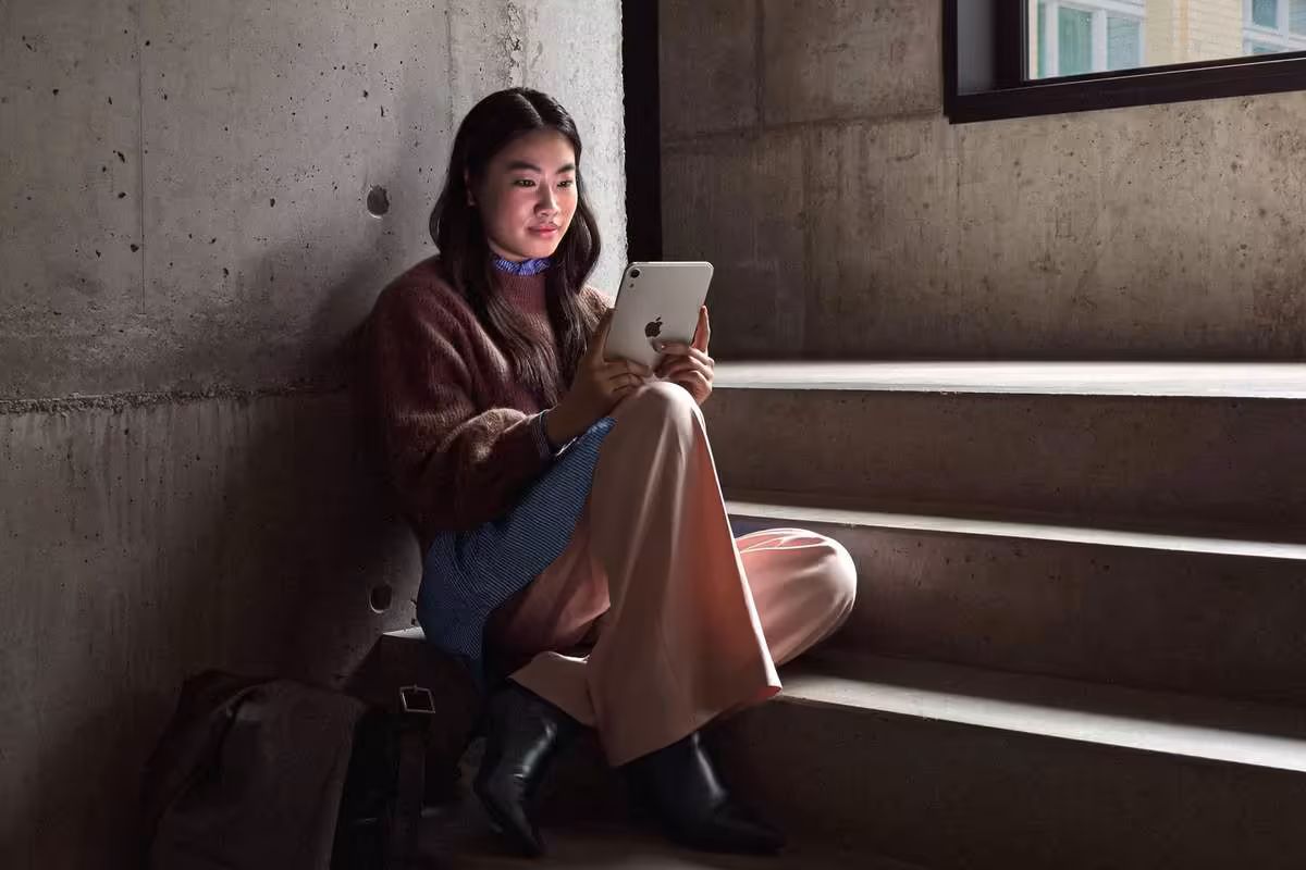 iPad mini : écran OLED 8,5 pouces, puce A20 Pro en 2 nm et certification IP67 6 Femme utilisant un iPad mini Apple assise sur des marches dans un intérieur sombre