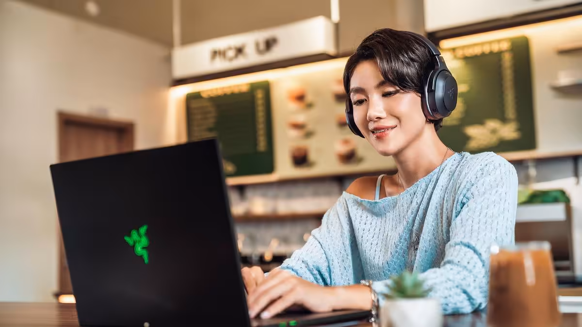 Razer Barracuda V2 Pro : ANC hybride, double connexion et 70 heures d’autonomie 6 Utilisatrice portant un casque Razer Barracuda V2 Pro devant un ordinateur portable Razer