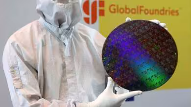 Employé GlobalFoundries en salle blanche tenant une tranche de silicium colorée devant le logo de l’entreprise