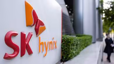 Logo SK hynix rouge et orange sur façade d’entreprise, avec passante floue devant le siège