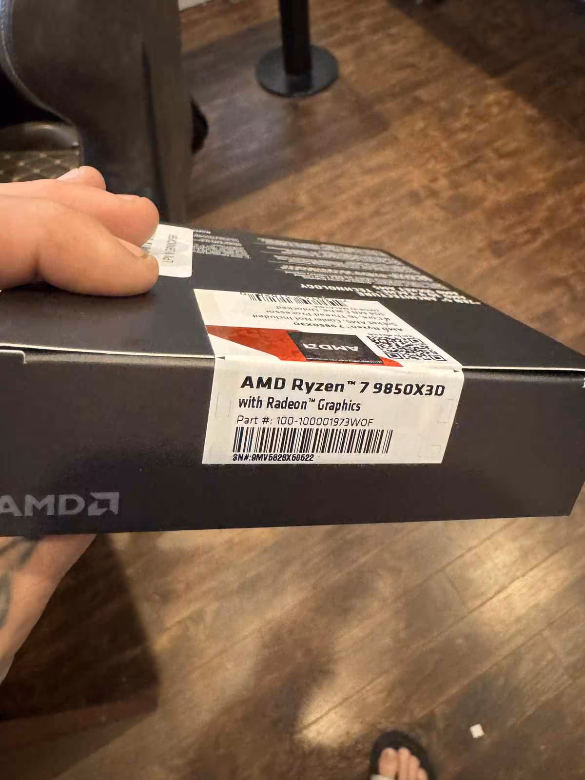 Main tenant une boîte AMD Ryzen 7 9850X3D avec étiquette produit Amazon visible
