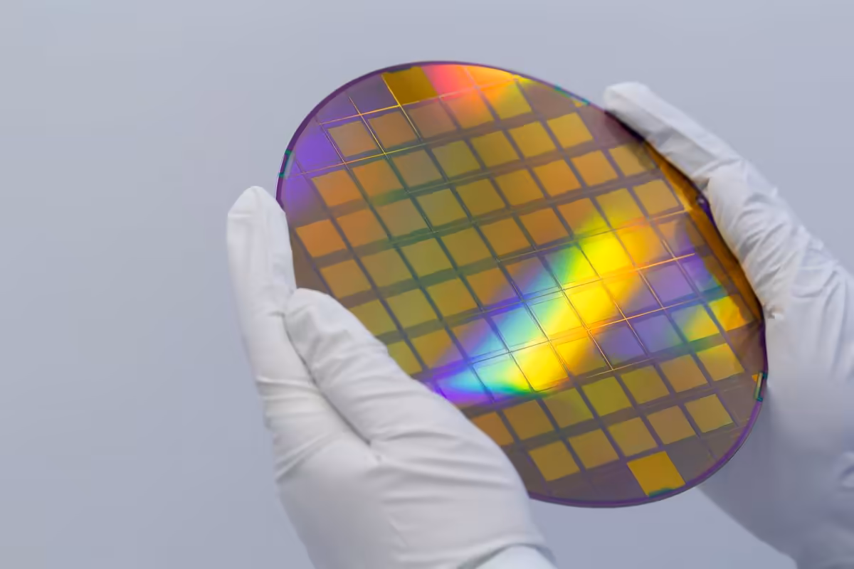 Wafer de silicium irisé tenu par des mains gantées, avec matrices de puces visibles